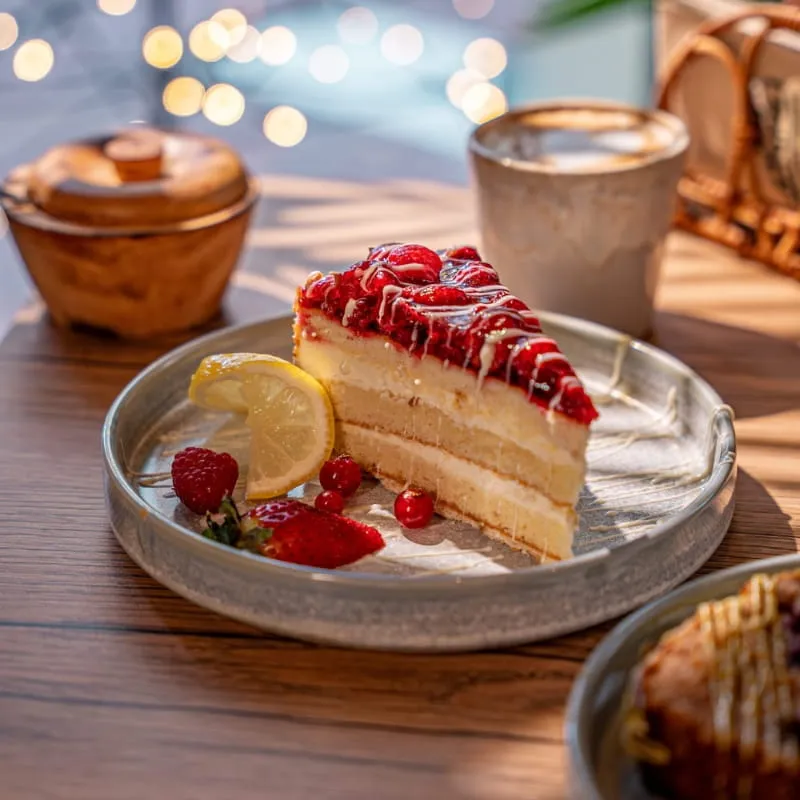 Stück Torte mit Beeren auf einem Keramikteller neben einer Tasse Kaffee